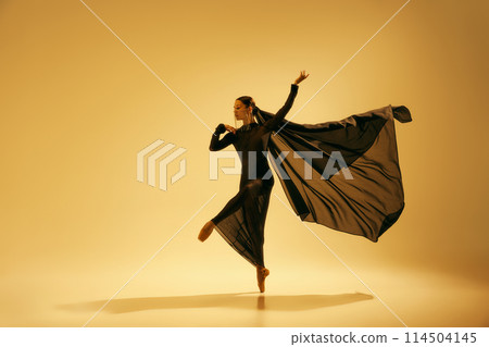 Poetry in motion. Beautiful woman, ballet dancer in elegant black dress performing against sand color background 114504145