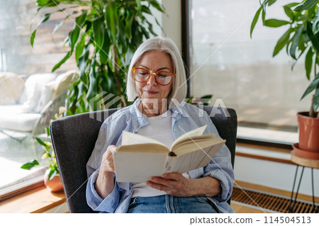 Beautiful mature woman reading book, feeling cozy and happy. Weekend activity for older woman, relaxing at home. 114504513