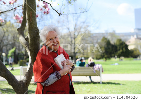 Beautiful elderly woman reading book outdoor, in park, having relaxing moment. Grandmother reading the bible in the cemetery. Beautiful elderly woman reading book outdoor, in park, having relaxing moment. Grandmother reading the bible in the cemetery. 114504526