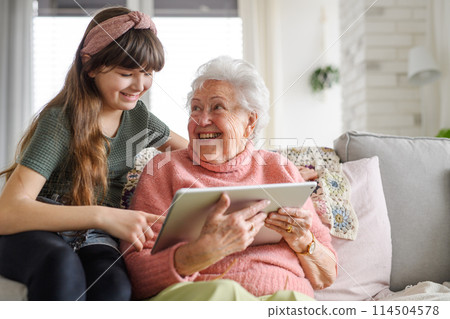 Grandmother with cute girl scrolling on tablet, girl teaching senior woman to work with technology, internet. Portrait of elderly woman spending time with granddaughter. Grandmother with cute girl scrolling on tablet, girl teaching senior woman to work with technology, internet. Portrait of elderly woman spending time with granddaughter. 114504578