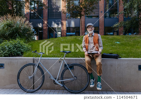 Stylish senior man sitting in the city park, holding tablet, shopping online. Concept of digital literacy and seniors using digital technologies. Stylish senior man sitting in the city park, holding tablet, shopping online. Concept of digital literacy and seniors using digital technologies. 114504671