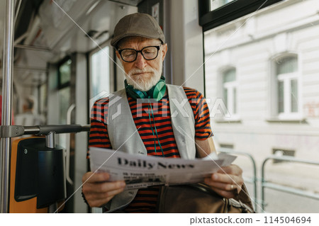Elderly man traveling through the city by bus, reading newspaper. Senior city commuter taking tram to grocery, using public transportation. Elderly man traveling through the city by bus, reading newspaper. Senior city commuter taking tram to grocery, using public transportation. 114504694