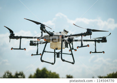 Close up of agricultural drone with spray nozzles and tank. Dron spraying crops, distribute pesticides, herbicides and fertilizers efficiently and precisely. Modern farming. 114504770