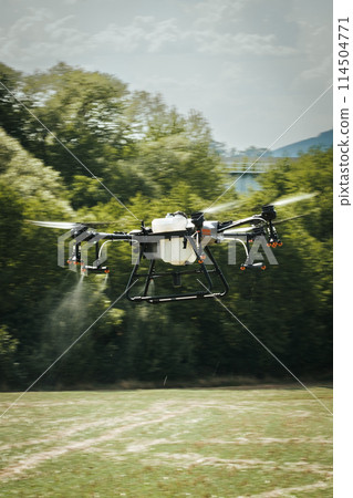 Agricultural drones spraying crops, distribute pesticides, herbicides and fertilizers efficiently and precisely. Aerial view of a drone moderning over farm fields, modern farming. 114504771