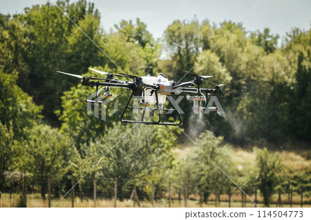 Agricultural drones spraying crops, distribute pesticides, herbicides and fertilizers efficiently and precisely. Aerial view of a drone moderning over farm fields, modern farming. Agricultural drones spraying crops, distribute pesticides, herbicides and fertilizers efficiently and precisely. Aerial view of a drone moderning over farm fields, modern farming. 114504773