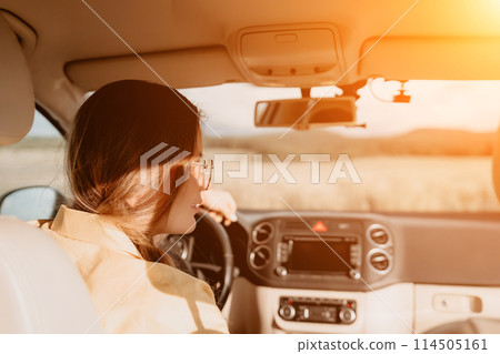A woman in a yellow shirt is driving a car. She is wearing glasses and has her hands on the steering wheel A woman in a yellow shirt is driving a car. She is wearing glasses and has her hands on the steering wheel 114505161