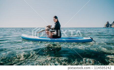 Sea woman sup. Silhouette of happy positive young woman with her dog, surfing on SUP board through calm water surface. Idyllic sunset. Active lifestyle at sea or river. Summer vacation with pets. Sea woman sup. Silhouette of happy positive young woman with her dog, surfing on SUP board through calm water surface. Idyllic sunset. Active lifestyle at sea or river. Summer vacation with pets. 114505242