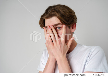 Young Man Covering His Face With His Hands Against a Neutral Background Young Man Covering His Face With His Hands Against a Neutral Background 114506799