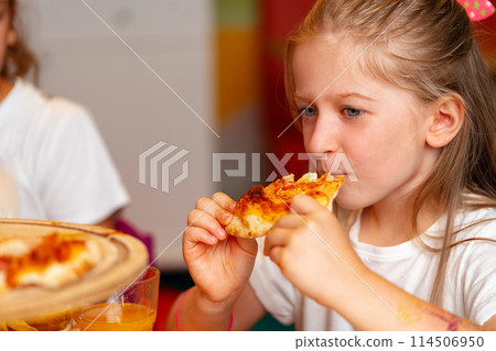 Young Girl Enjoying a Slice of Pizza at a Birthday Party Indoors Young Girl Enjoying a Slice of Pizza at a Birthday Party Indoors 114506950