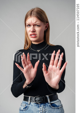Young Woman Expressing Discomfort and Disapproval With Hands Up in Studio 114507105