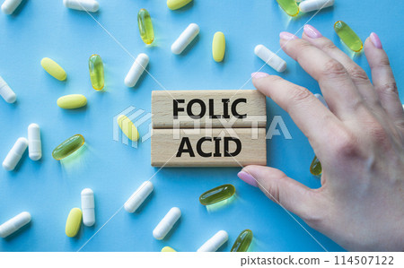 Folic acid symbol. Wooden blocks with words Folic acid. Beautiful blue background with pills. Doctor hand. Medicine and Folic acid concept. Copy space. Folic acid symbol. Wooden blocks with words Folic acid. Beautiful blue background with pills. Doctor hand. Medicine and Folic acid concept. Copy space. 114507122