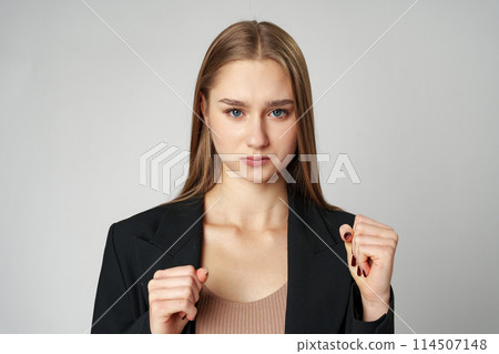 A young woman stands confidently against a neutral background with clenched fists A young woman stands confidently against a neutral background with clenched fists 114507148