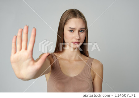 Young Woman in Fashionable Outfit Standing Against a Neutral Backdrop Showing Stop Gesture Young Woman in Fashionable Outfit Standing Against a Neutral Backdrop Showing Stop Gesture 114507171