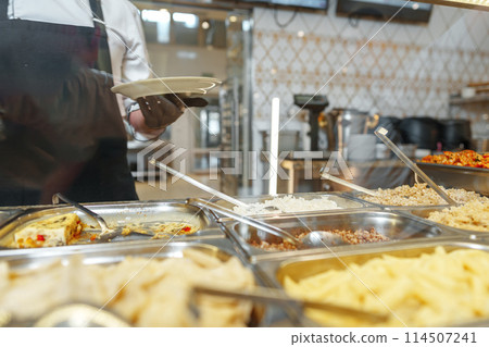 Chef Serving Freshly Cooked Dishes at a Restaurant Buffet During Lunchtime 114507241