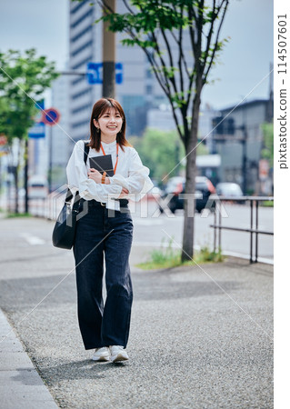 A young woman walking with a notebook on her chest 114507601
