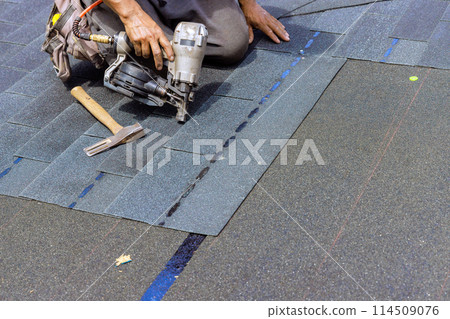Installing new bitumen shingles using an air nail gun on roof of house 114509076