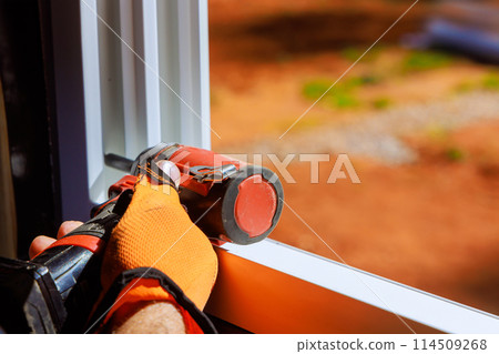 Construction worker is installing plastic windows with screwdriver in newly constructed home 114509268
