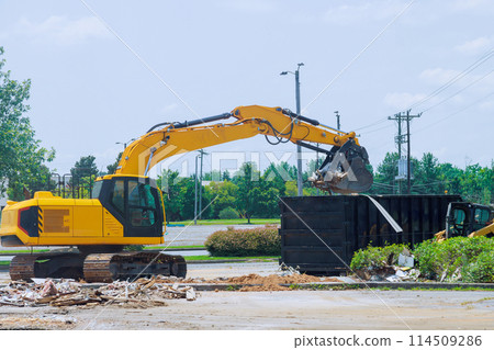 On construction site, an excavator loads construction concrete waste into disposal container 114509286
