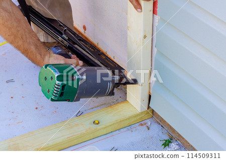 Working as framer, using an air nail hammer to install beams in wooden frame Working as framer, using an air nail hammer to install beams in wooden frame 114509311