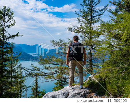 a traveler with a backpack stands on a mountain against the backdrop of Lake Attersee, Austria a traveler with a backpack stands on a mountain against the backdrop of Lake Attersee, Austria 114509403