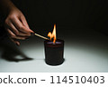 a burning match in the hand of a woman sets fire to a candle standing on the table 114510403