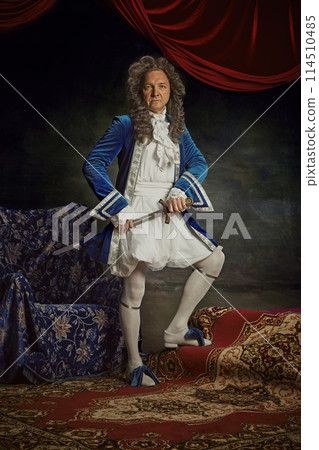 Medieval person, senior man posing wearing old-fashioned clothes posing with sword against vintage studio background. 114510485
