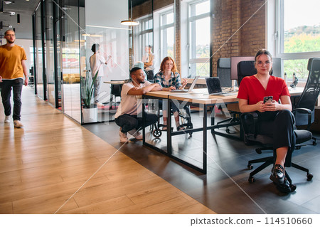 A diverse group of business professionals collaborates in a modern startup coworking center, utilizing a mix of paper-based and technological tools such as mobile phones and computers  114510660