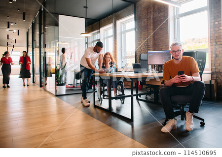 A diverse group of business professionals collaborates in a modern startup coworking center, utilizing a mix of paper-based and technological tools such as mobile phones and computers to collectively 114510695
