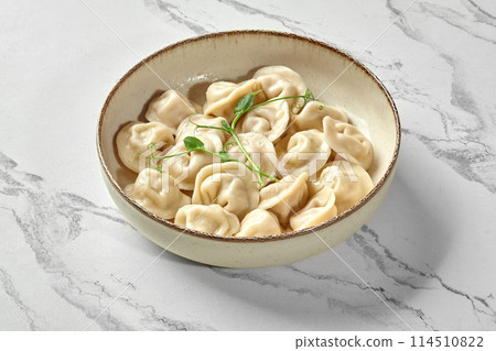 Bowl of freshly boiled dumplings with greens on marbled surface 114510822