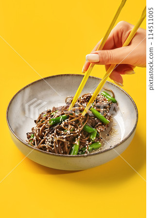 Female hand taking beef soba noodle with chopsticks from bowl Female hand taking beef soba noodle with chopsticks from bowl 114511005