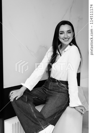 Happy smiled woman in formal denim style with white shirt sitting on chair. 114511174