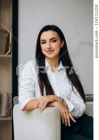 Portrait of businesswoman in whiter shirt sitting in chair in office hall. Finance manager  114511208