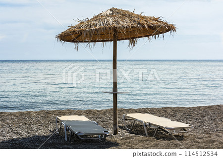 On the beach of pebbles is an umbrella and two sunbeds On the beach of pebbles is an umbrella and two sunbeds 114512534