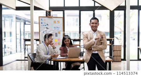 Smiling confident businessman looking at camera and standing in an office at team meeting. Portrait of confident businessman with colleagues in boardroom 114513374