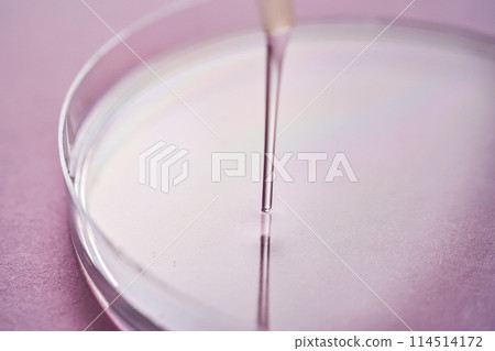 Serum or cosmetic oil flows into a transparent bowl on a purple background. Serum or cosmetic oil flows into a transparent bowl on a purple background. 114514172