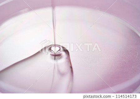 Serum or cosmetic oil flows into a transparent bowl on a purple background. Serum or cosmetic oil flows into a transparent bowl on a purple background. 114514173