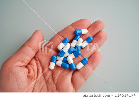 A hand holds a handful of white and blue pills on a blue background. A hand holds a handful of white and blue pills on a blue background. 114514174
