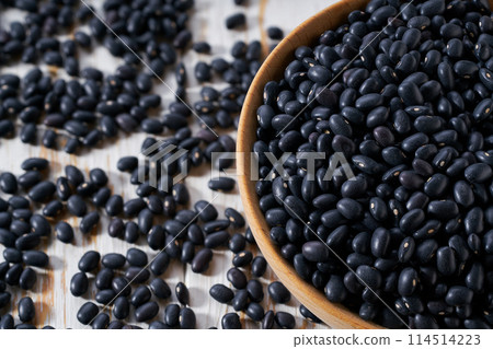 Organic black beans are scattered out of the wooden bowl on a light table, selective focus. Organic black beans are scattered out of the wooden bowl on a light table, selective focus. 114514223