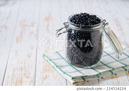 Raw black beans in glass storage jar on a white wooden table. 114514224