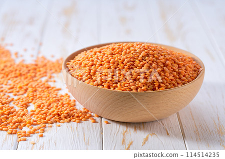 Organic red lentils in a wooden bowl on a white wooden table. 114514235
