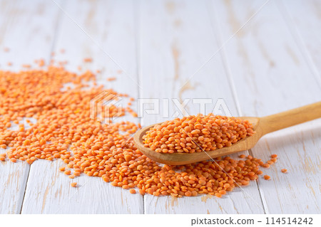 Raw red lentils crumble from in a wooden spoon on a white wooden table. Raw red lentils crumble from in a wooden spoon on a white wooden table. 114514242