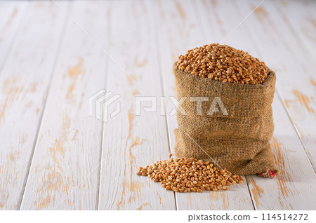 Raw organic wheat in sack on a light table, selective focus. Raw organic wheat in sack on a light table, selective focus. 114514272