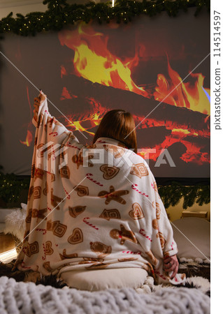 Young beautiful woman from behind sit on bed with cake man on wrap in room decorated for celebrating the new year and christmas festive mood on projector fireplace image background 114514597