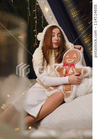 Merry young fun woman wearing white warm sweater hat posing hold ginger cookie man pillow studio portrait. Happy New Year celebration holiday concept Merry young fun woman wearing white warm sweater hat posing hold ginger cookie man pillow studio portrait. Happy New Year celebration holiday concept 114514608