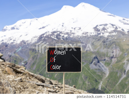 WOC women of color symbol. Concept words WOC women of color on beautiful yellow blackboard. Beautiful mountain Elbrus background. Business WOC women of color social issues concept. Copy space. 114514731