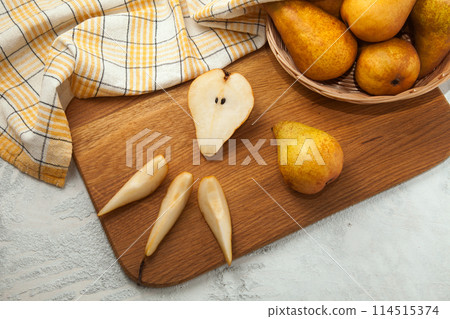 Cutting board with whole and slices pears, wicker basket and yellow kitchen towel on white wooden background.. Cutting board with whole and slices pears, wicker basket and yellow kitchen towel on white wooden background.. 114515374