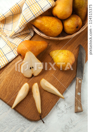 Cutting board with whole and slices pears, wicker basket and yellow kitchen towel on white wooden background.. 114515375