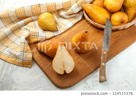 Cutting board with whole and halves pears, wicker basket and yellow kitchen towel on white wooden background.. Cutting board with whole and halves pears, wicker basket and yellow kitchen towel on white wooden background.. 114515376