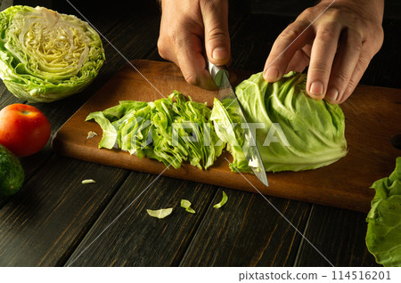 The cook cuts young fresh cabbage with a knife to prepare a salad with vegetables. Low key concept for preparing a vegetarian dish The cook cuts young fresh cabbage with a knife to prepare a salad with vegetables. Low key concept for preparing a vegetarian dish 114516201