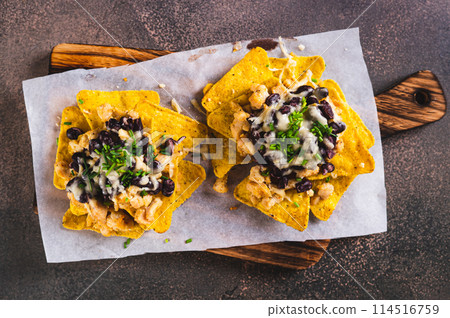 Close up of mexican baked nachos with chicken, black beans and cheese on a board top view Close up of mexican baked nachos with chicken, black beans and cheese on a board top view 114516759